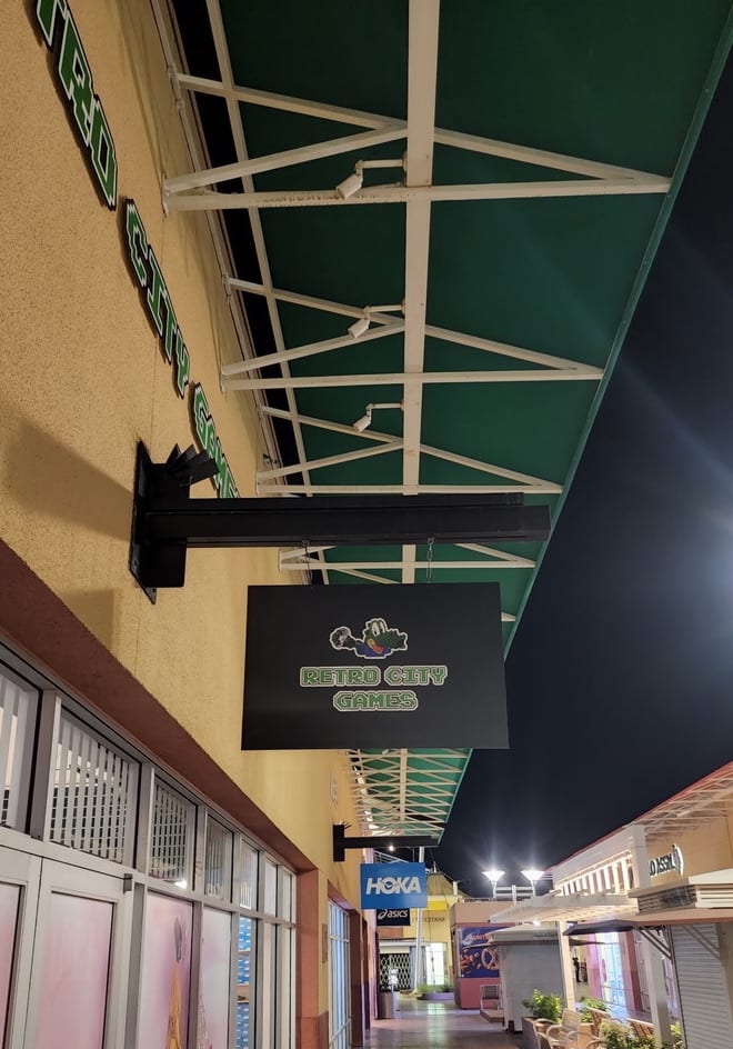 hanging blade sign las vegas Retro City Games hanging blade sign under an outdoor mall walkway, with green letters on the wall above