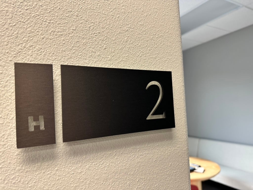 room number sign Room number sign: a silver 2 on a black panel beside a room letter plate